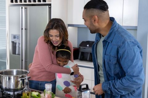 Parents hugging daughter in kitchen while preparing meal, warm family bonding moment
