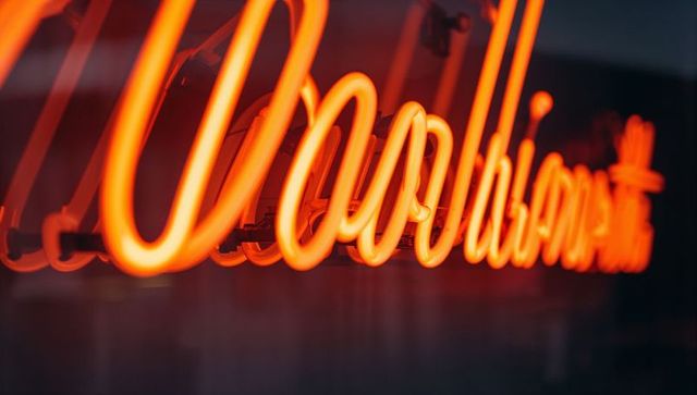 Glowing orange cursive neon sign casting warm reflections on glass panel