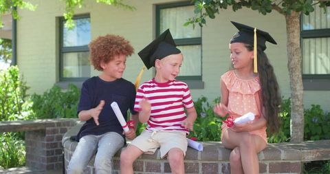 Smiling children celebrating kindergarten graduation wearing caps and holding diplomas