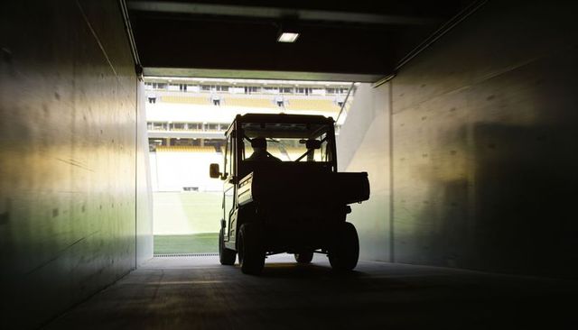 Driving utility vehicle exiting tunnel into stadium with silhouetted operator