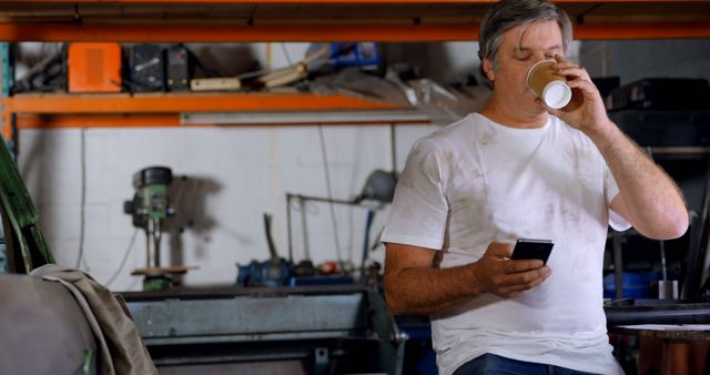 Middle-Aged Man Drinking Coffee and Using Smartphone in Workshop - Download Free Stock Images Pikwizard.com