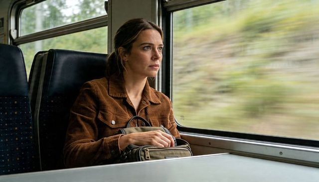 Pensive woman traveling by train holding bag and gazing out window at passing landscape