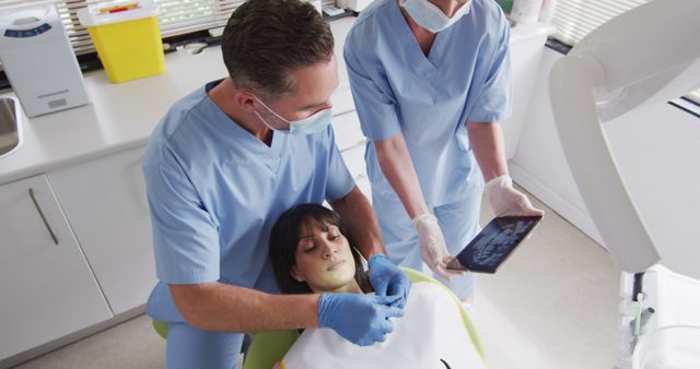 Dentists working on patient in modern dental clinic. Dental professionals performing examination, checking dental x-rays. Can be used for healthcare, dental care, clinic promotions, and medical training materials.