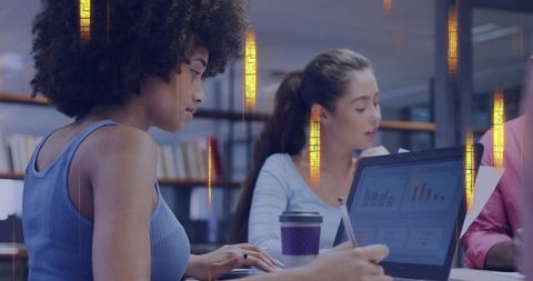 Young women collaborating on laptop, analyzing charts and taking notes in coworking space