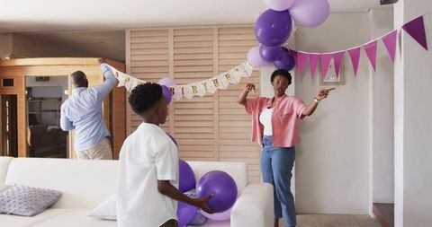 African American family decorating living room with purple balloons and birthday banner