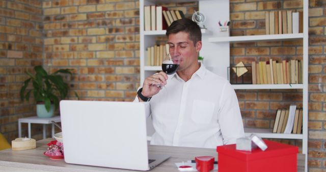 Relaxed man drinking wine at home office while using laptop - Download Free Stock Images Pikwizard.com