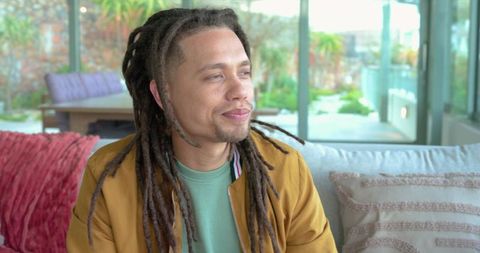 Man with dreadlocks relaxing on sofa near glass doors in contemporary living room