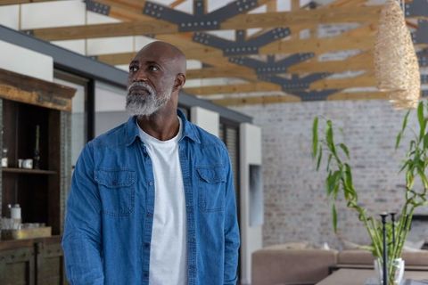 Senior african man gazing upward in rustic industrial loft wearing denim shirt white tee