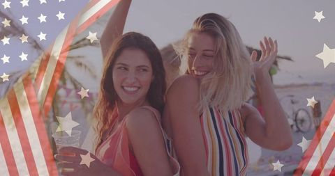Smiling women posing back-to-back on beach with us flag overlay, summer friendship