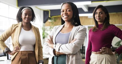 Confident diverse women leaders standing with arms crossed in modern sunlit office
