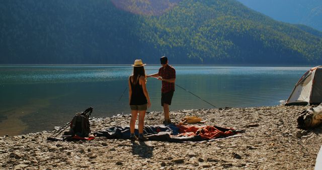 Couple camping by a serene mountain lake, setting up a picnic area and tent. Ideal for marketing travel and outdoor adventure activities, promoting camping products, or illustrating an article on outdoor leisure. Perfect for use in hiking and camping blogs or travel advertisements highlighting natural landscapes.