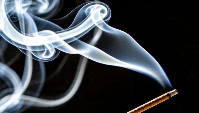 Curling bluish smoke rising from lit incense stick with glowing ember