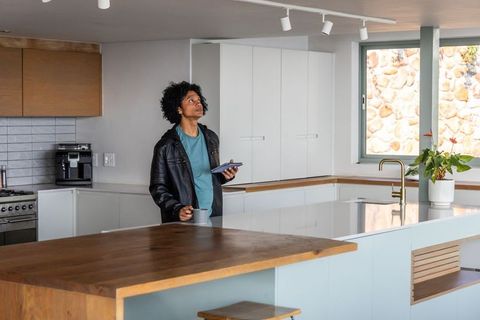 African american man standing at modern kitchen island holding tablet and coffee mug glancing up