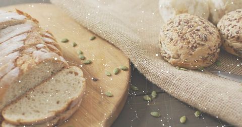 Rustic sliced artisan bread and seeded rolls on wooden board with burlap and pumpkin seeds