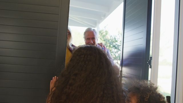 Cheerful grandparents are warmly welcomed at the front door by their diverse grandchildren. This video is perfect for illustrating themes such as family bonds, love, warmth, and multiethnic family dynamics. It can be used on websites, brochures, and advertisements highlighting family values, intergenerational connections, and diversity.