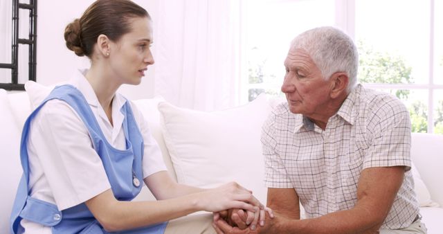 Nurse in uniform providing emotional support to elderly man sitting on couch at home. Ideal for use in healthcare, senior living, elder care, nursing services, and caregiving promotional materials. Highlights empathy, professional care, and at-home assistance.