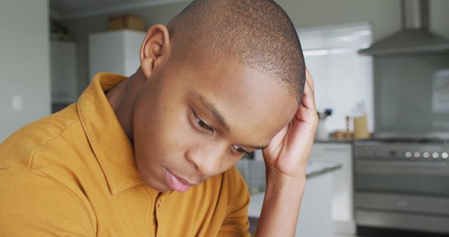 This image captures a man in a kitchen, reflecting serious thoughts and emotions. It is suitable for use in articles about stress, mental health, personal struggles, or emotional well-being. The indoor setting can also work for lifestyle blogs and counseling services, effectively illustrating moments of worry or contemplation.