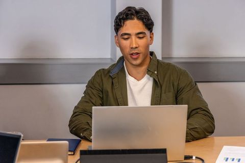 Focused asian man working on laptop at meeting table, concentrating on remote work