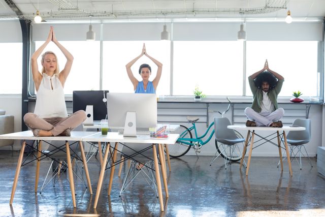 Executives practicing yoga on desks in a modern office environment. This image can be used to promote workplace wellness programs, corporate health initiatives, stress relief techniques, and mindfulness practices in professional settings. Ideal for articles, blogs, and marketing materials related to employee well-being and office fitness activities.