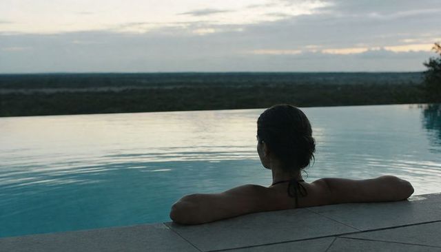 Woman relaxing at infinity pool during twilight with horizon views, calm water, solitude