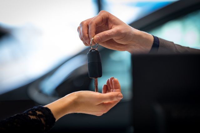 Salesman handing car key to customer in showroom. Ideal for use in automotive sales, car dealership promotions, business transactions, and customer service materials.