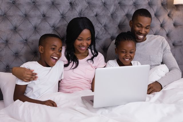 Happy family using laptop while sitting together on bed at home