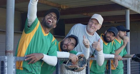 Smiling baseball teammates with coach in dugout giving thumbs up