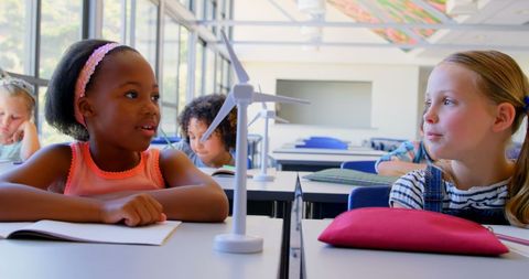 children having discussions at their desks in a bright, modern classroom setting conveys the essence of learning through interaction. the visible engagement among students makes it ideal for educational themes, teaching materials, school recruitment ads, or articles focusing on diversity and modern education approaches.