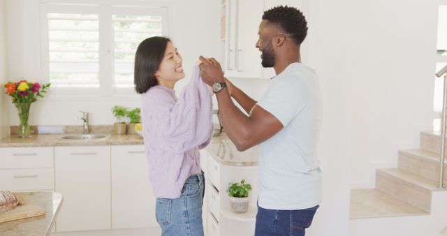 Happy diverse couple holding hands and dancing in kitchen. Spending quality time at home concept.
