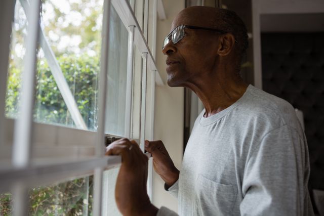 Senior man wearing eyeglasses while looking out through window at home