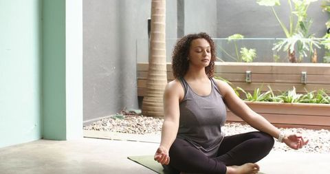 Curly-haired woman meditating on patio yoga mat practicing mindfulness and stress relief outdoors