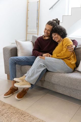 Couple cuddling on sofa in modern minimalist living room wearing cozy sweaters smiling