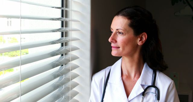 Female Doctor Looking Through Window with Contemplative Expression - Download Free Stock Images Pikwizard.com