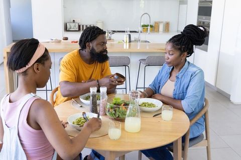 African american family sharing green pasta and salad while dining at wooden kitchen table