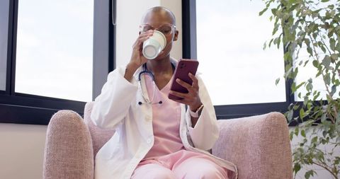 Doctor sipping coffee while checking smartphone in modern clinic lounge