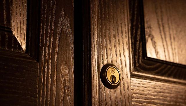 Brass escutcheon and keyhole on dark wooden door revealing warm grain and dramatic light