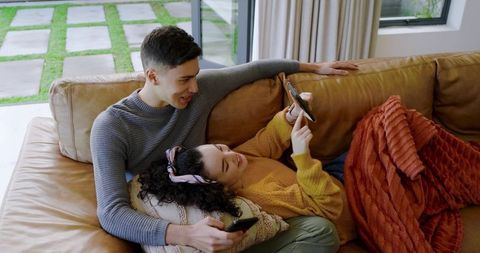 Happy Couple Embracing Technology Relaxing on Leather Sofa