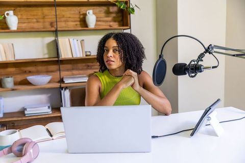 African american creator recording home podcast with microphone, laptop, modern workspace