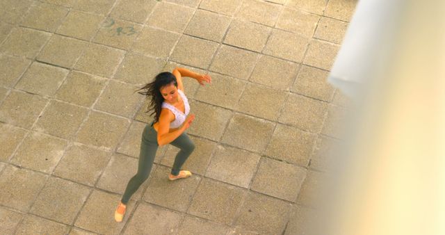 Female dancer practices routine on urban street with concrete pavement. She wears green pants and a velvet mesh costume. Ideal for fitness, dance, urban lifestyle, and outdoor sports themes.