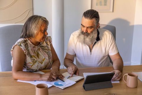 Senior couple reviewing finances using tablet and printed charts for retirement planning