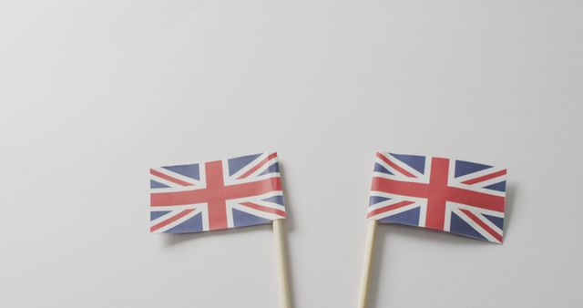 Two small United Kingdom flags on sticks displayed on a plain light background. Ideal for illustrating British patriotism, national celebrations, cultural events, or educational materials. Suitable for use in articles about the UK, promotional materials for British-themed events, or as part of graphic designs related to British culture.