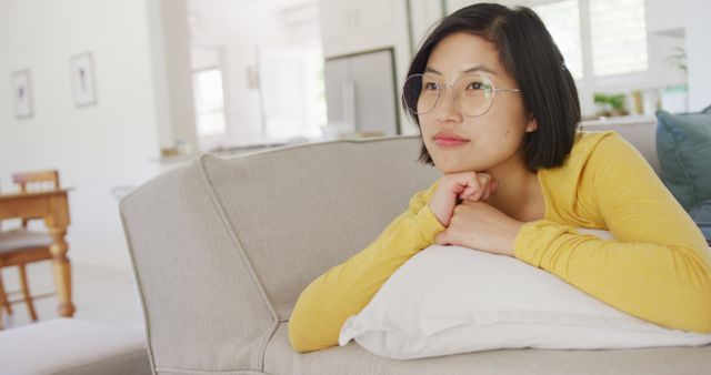Happy asian woman lying on couch in living room. Spending quality time at home concept.
