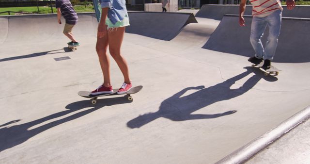 Low section of caucasian woman and two male friends skateboarding on sunny day. hanging out at skatepark in summer.
