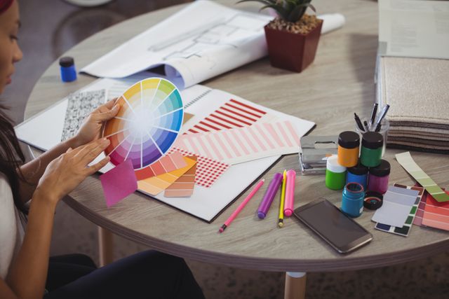 Businesswoman holding color swatch at desk in creative office. Ideal for illustrating concepts of creativity, design, and professional work environments. Useful for articles on interior design, creative processes, and office productivity.