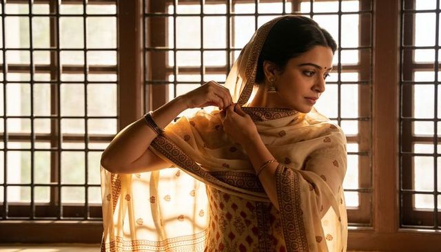 Adjusting cream-gold dupatta, indian woman draping traditional attire by lattice window