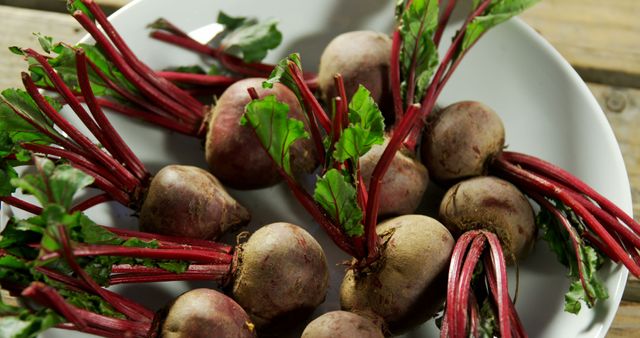 Fresh organic beetroots with lush greens arranged in a white bowl on a wooden table. Ideal for articles about healthy eating, organic farming, and plant-based recipes. Suitable for sustainable lifestyle stories and dietary guides featuring nutritious ingredients.