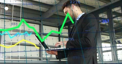 Executive in Suit Analyzing Financial Charts on Laptop in Industrial Warehouse