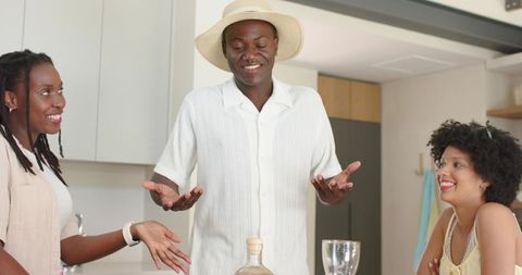 African american friends laughing and chatting at bright modern kitchen counter with straw hat