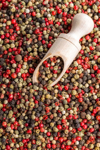 Top view of a variety of colorful mixed peppercorns, including red, black, and white, with a wooden scoop placed on top. Perfect for use in culinary blogs, websites about spices and cooking, seasoning company advertisements, or any creative project related to food and flavors.