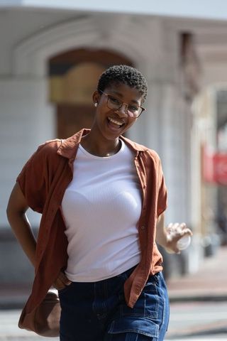Laughing young african woman wearing glasses, rust shirt and denim on sunlit urban street